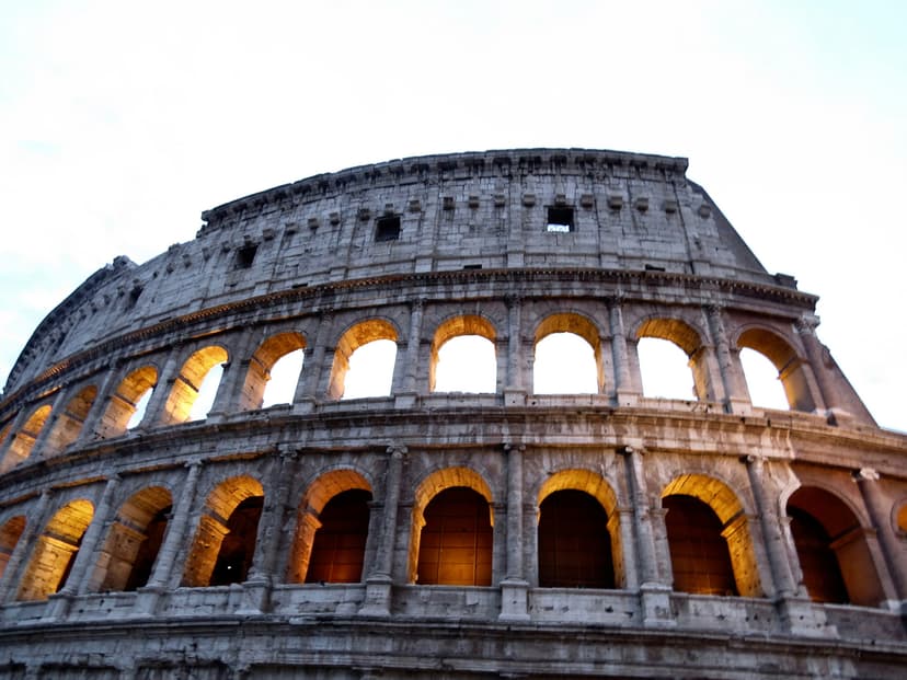 Roman Colosseum illuminated at dusk with ancient stone architecture and tourists walking nearby